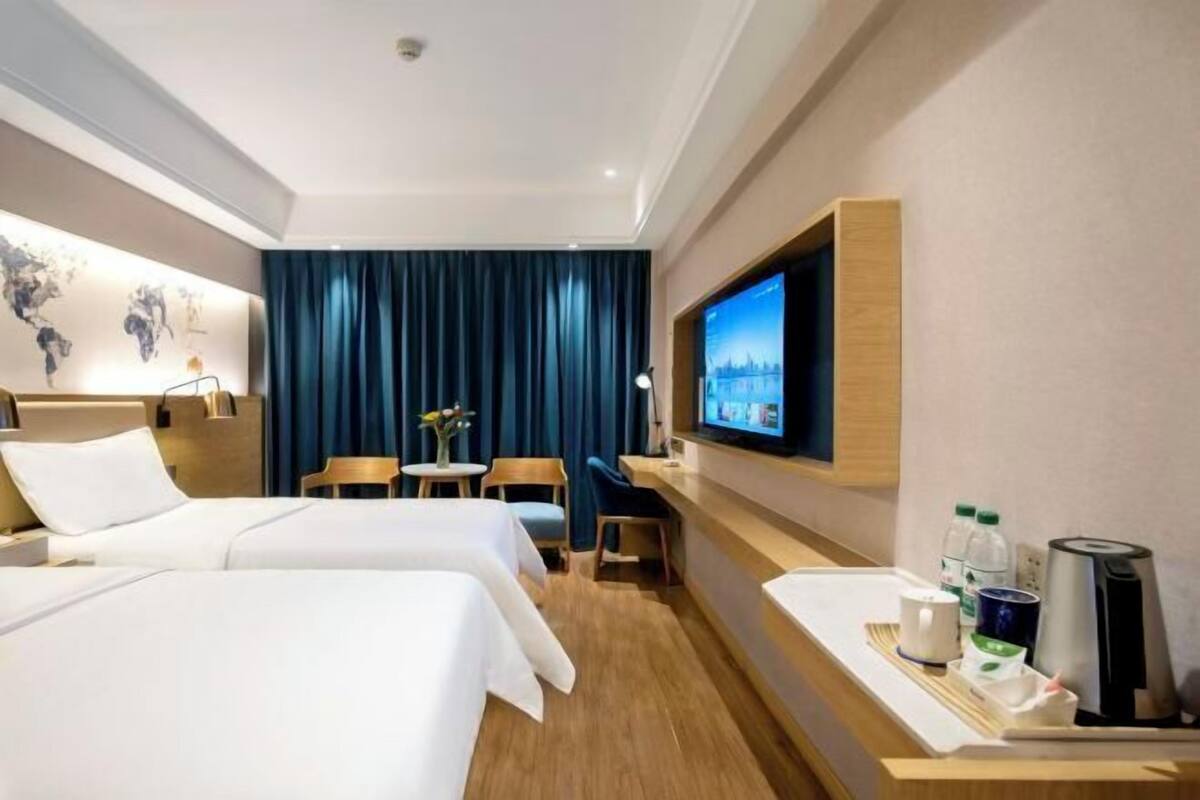 A hotel room with two beds, a TV, a desk with a coffee maker, and a small table with a vase.