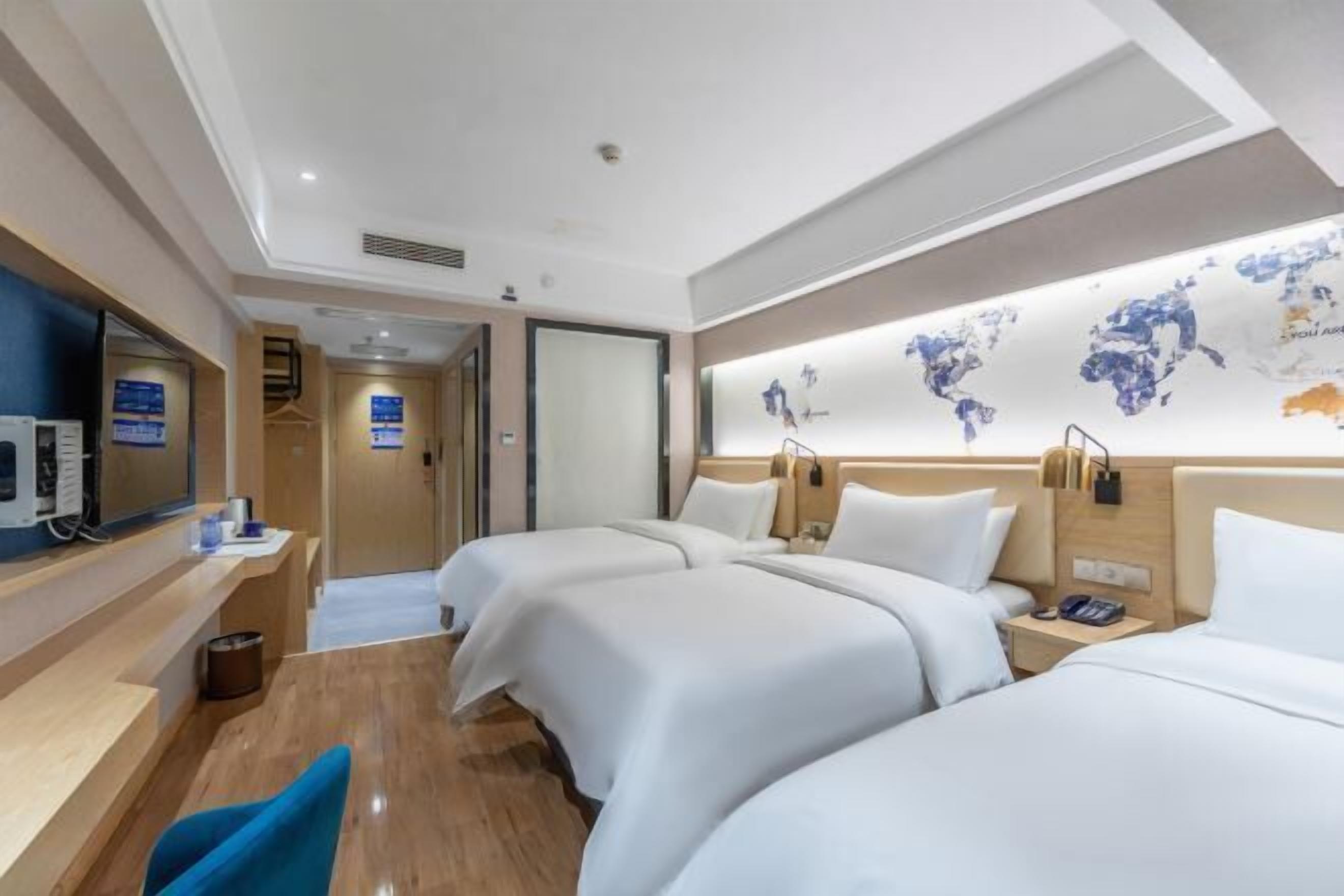 Habitación de hotel con tres camas, un televisor, un mapa mundial en la pared y piso de madera.