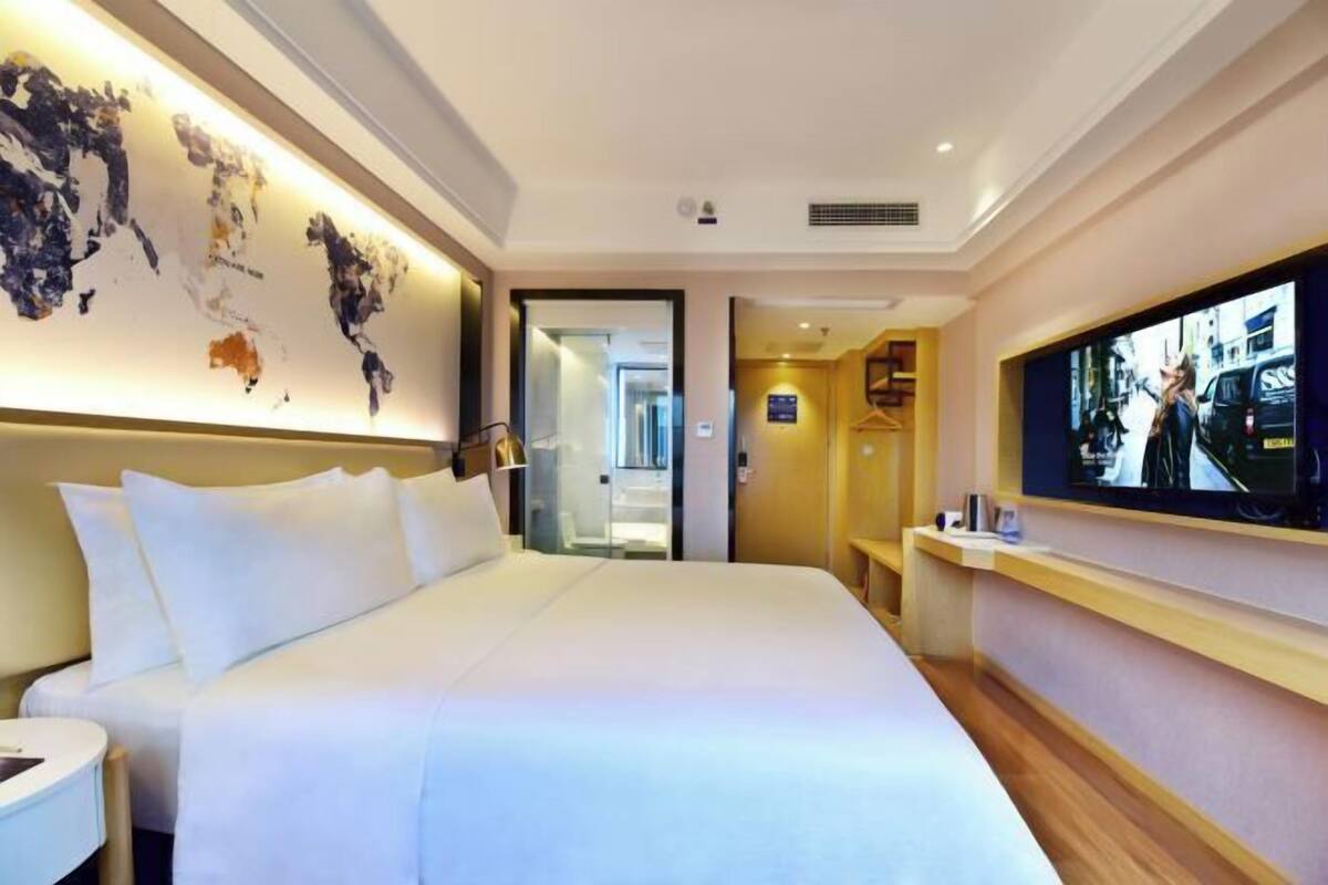 A hotel room with a large bed, a television on the wall, and a world map artwork.