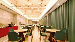 A modern dining area with round tables and green chairs, a red counter, and a ceiling with geometric light fixtures. - Wanhou Academy of Fine Arts Hotel (Yiyang Xiufeng Park Branch) (Yiyang)