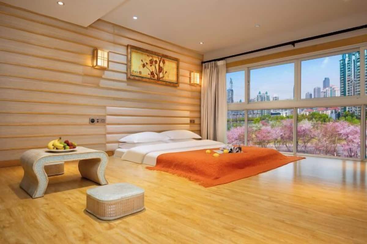 Una habitación de hotel moderna con un ventanal grande, una cama, una mesita con fruta y vistas a la ciudad.