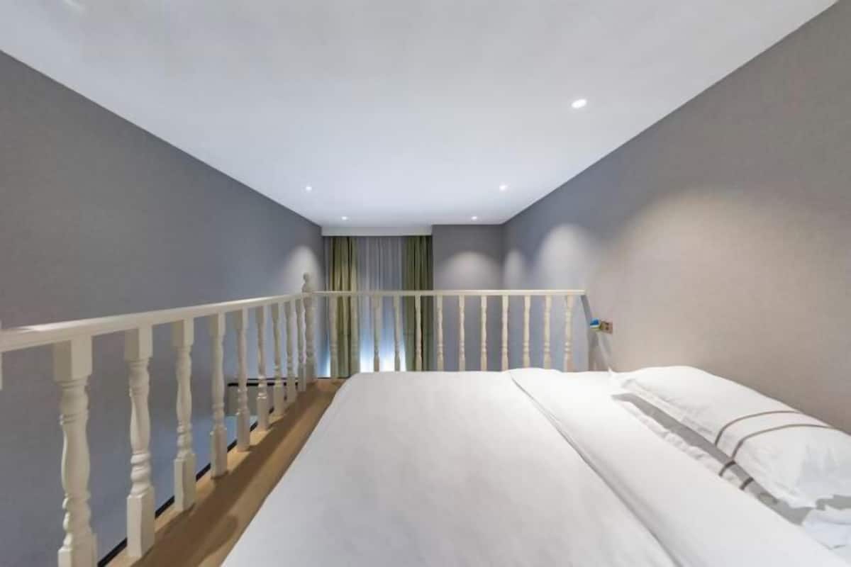 Un dormitorio con cama, barandilla blanca y vista a una escalera.