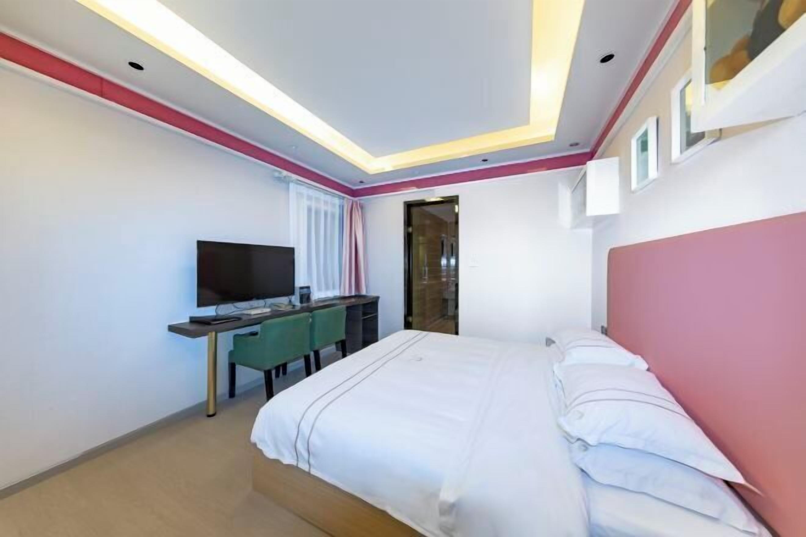 A modern hotel room with a bed, a desk with a computer, a TV, and a large window.