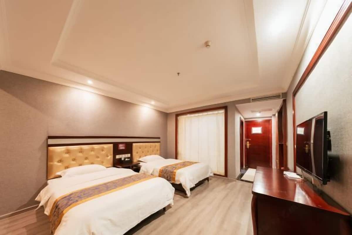 Habitación de hotel con dos camas, un escritorio de madera, un televisor de pantalla plana y una puerta que da a un pasillo.