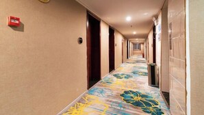Ein Hotelgang mit einem floralen Teppich, Türen und einem Rauchmelder an der Wand.