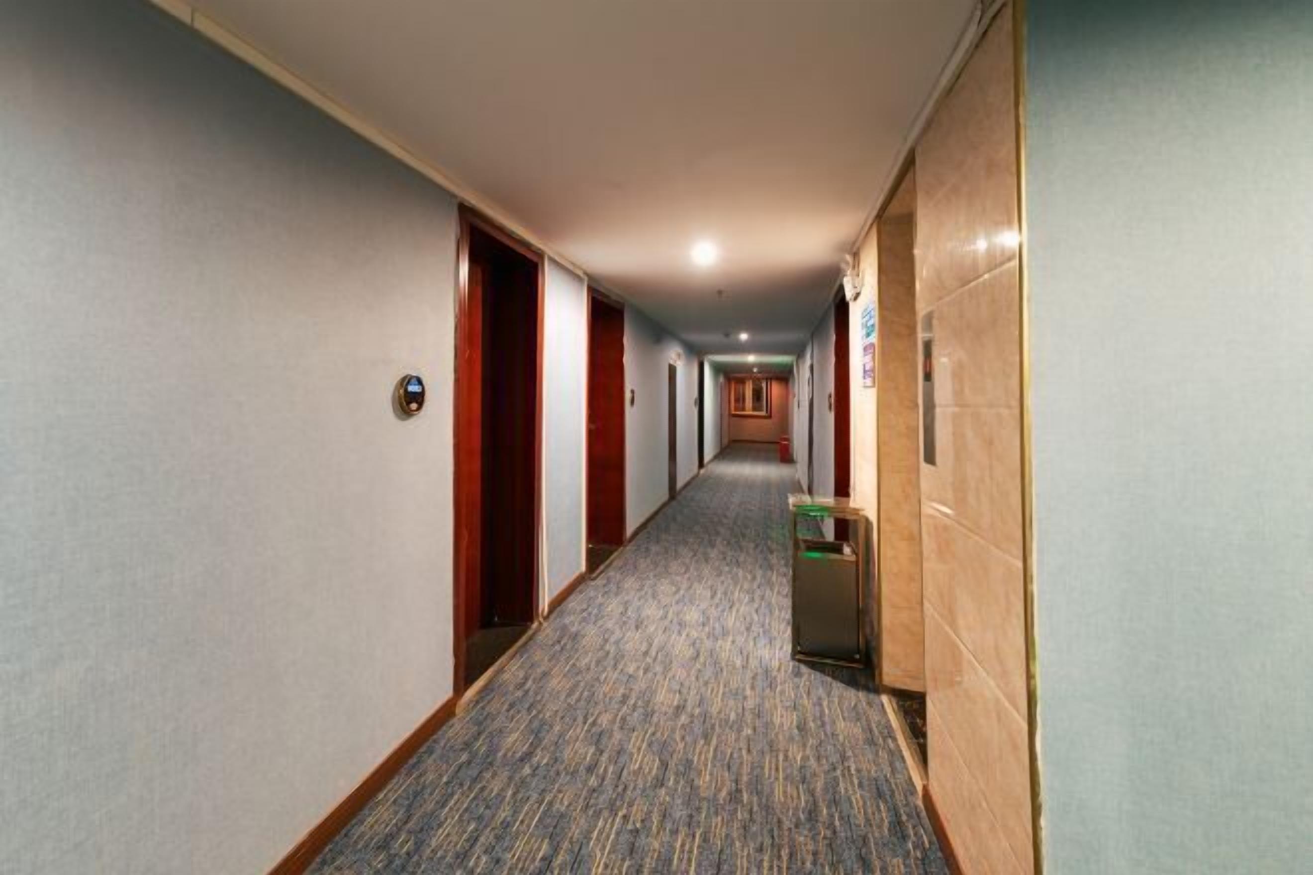 Ein Hotelkorridor mit Teppichböden, Holztüren und einem Mülleimer.