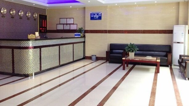 A hotel reception area with a reception desk, a sofa, a coffee table, and a potted plant. - Huaxuan Hotel (Jiangmen)