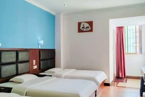 Habitación de hotel con dos camas, una pared azul, un cabecero de madera, un cuadro enmarco, una ventana con cortinas y una mesita.