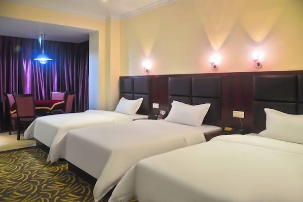 A hotel room with three beds, a dining area with a table and chairs, and a curtain backdrop. - Huaxuan Hotel (Jiangmen)