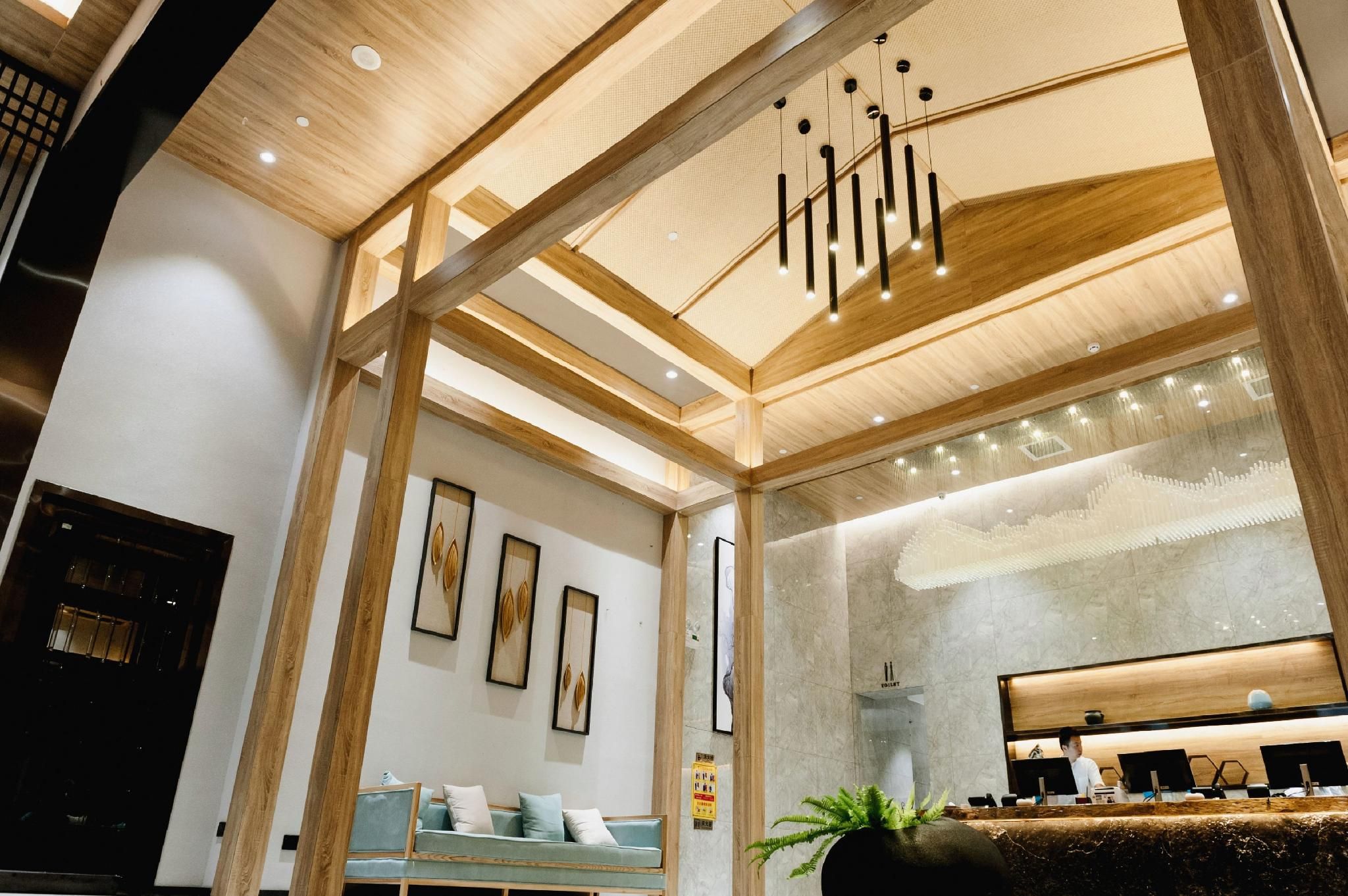 Un moderno vestíbulo de hotel con una recepción, un área de descanso y un espejo grande que refleja el interior.