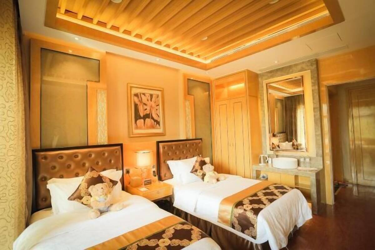 Une chambre d’hôtel avec deux lits, un grand miroir, une coiffeuse avec un lavabo et un plafond recouvert de lambris en bois.