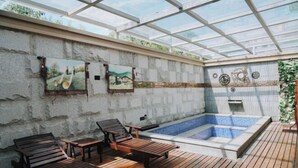 Ett takförsett utomhusområde med en bubbelpool, träloungestolar och en stenmur med konstverk.