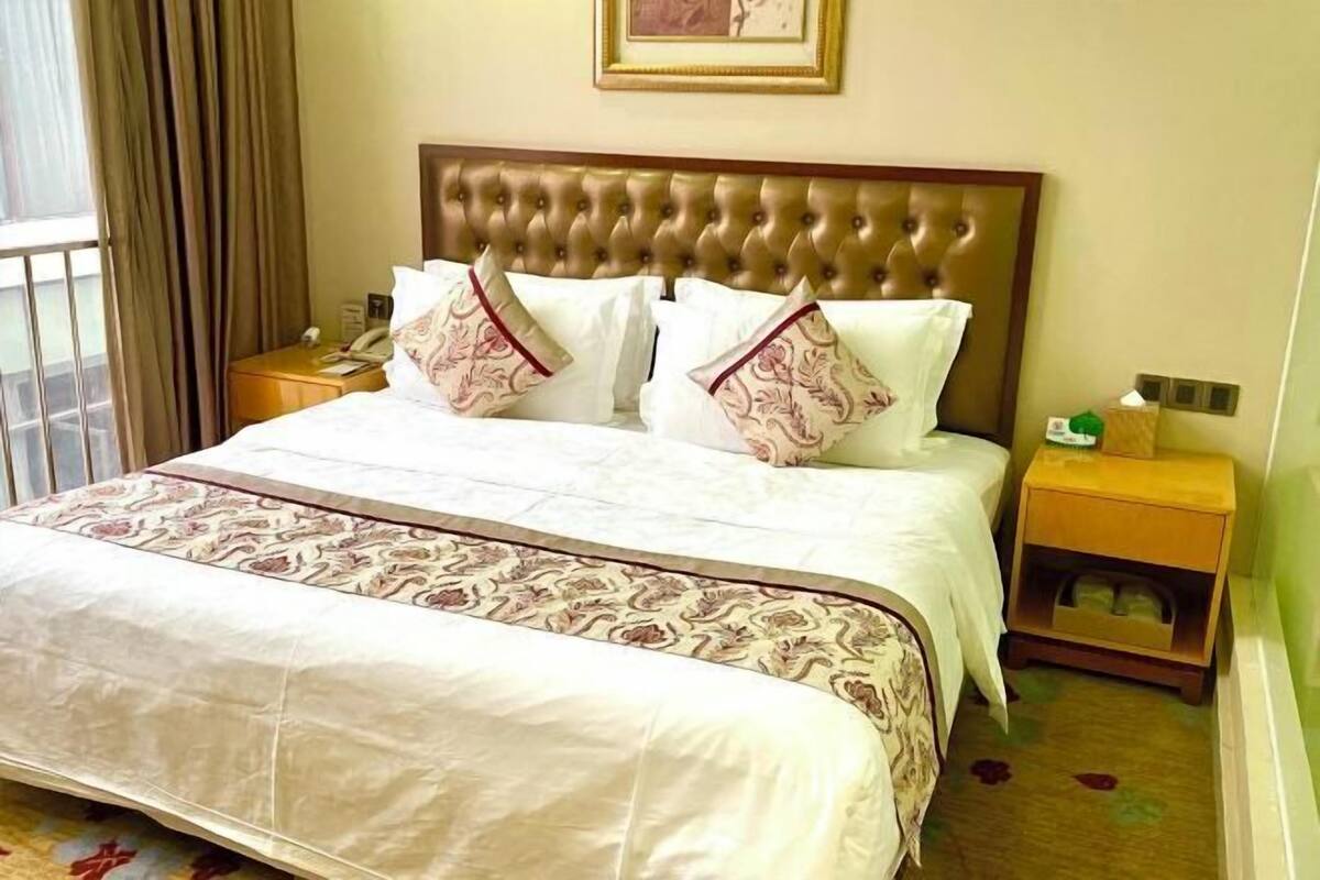 Une chambre d’hôtel avec un grand lit, une tête de lit capitonnée, une table de chevet avec une lampe et une petite table de nuit avec une boîte de mouchoirs.