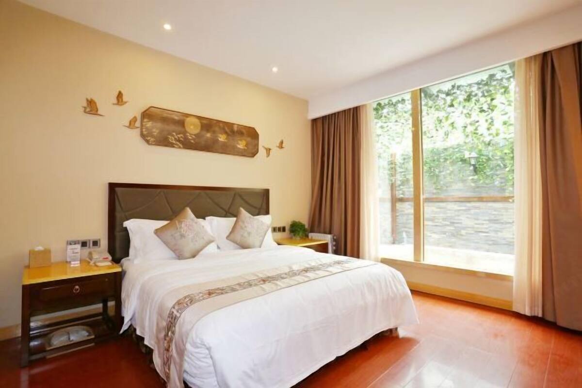 Une chambre d’hôtel avec un grand lit, une table de chevet, une horloge murale et une fenêtre avec des rideaux.