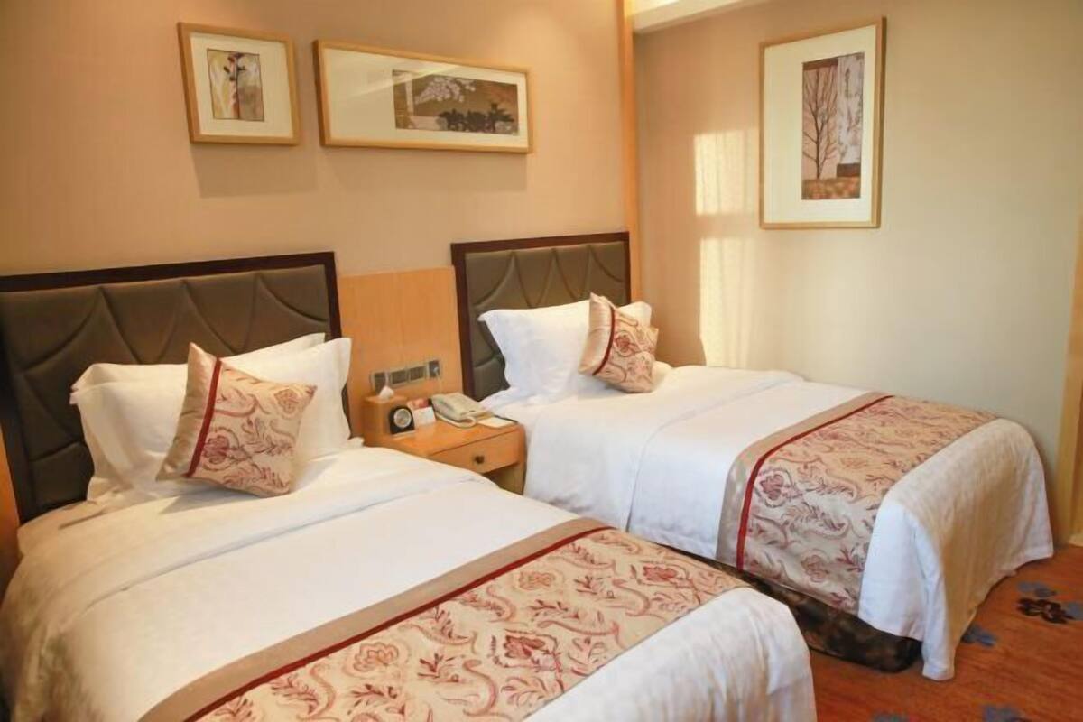 Une chambre d’hôtel avec deux lits, chacun doté d’une tête de lit, d’une table de chevet avec une lampe et de tableaux encadrés accrochés au mur.