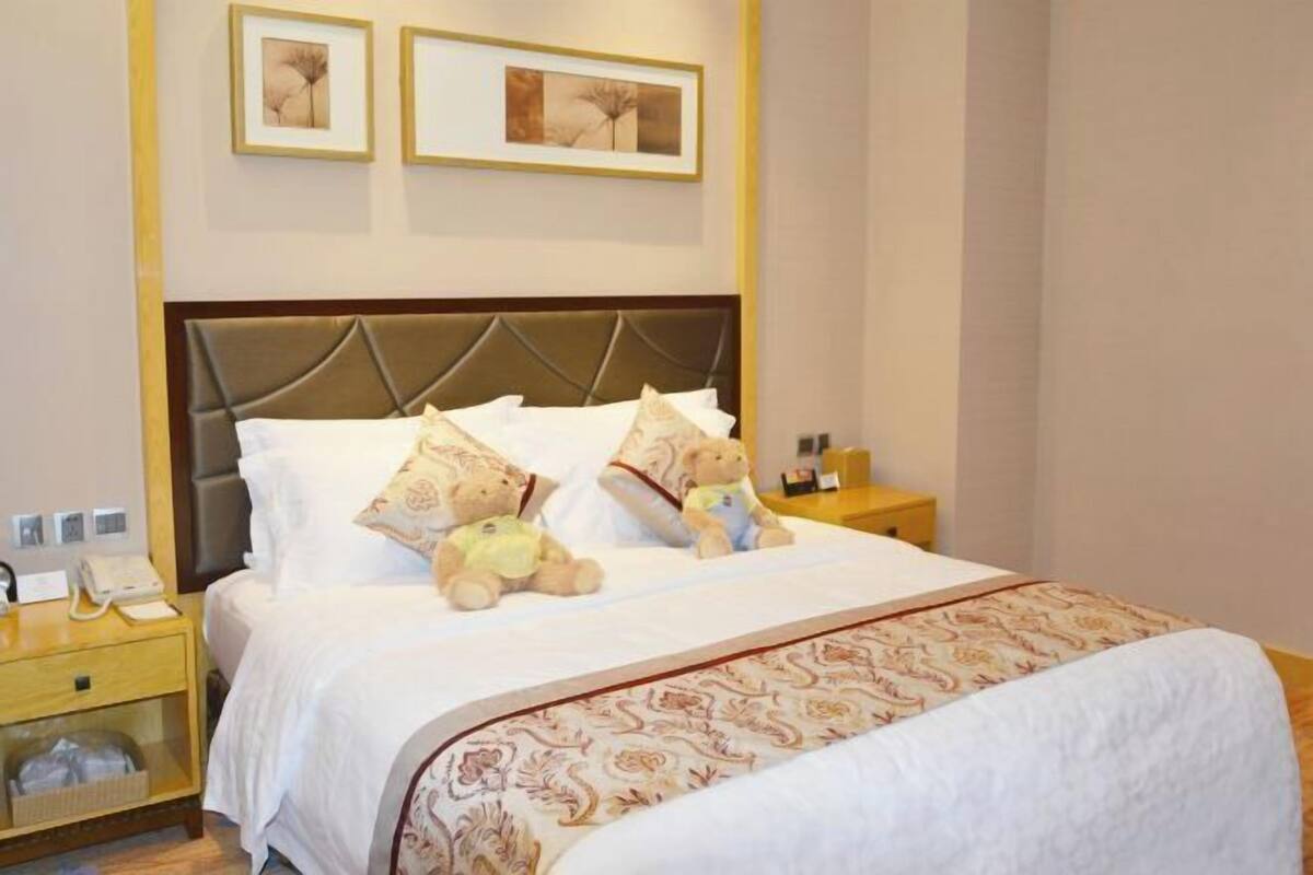 Un lit bien fait, recouvert d’une couvre-lit à motifs, deux tableaux encadrés accrochés au mur et une table de chevet avec une lampe et un téléphone.