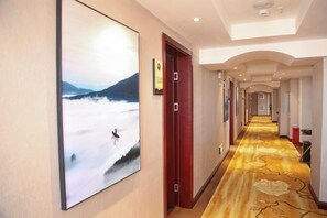 A hotel hallway with a carpeted floor, a framed picture on the wall, and a door with a sign. - Meishan Hotel (County Government Store) (Daming)