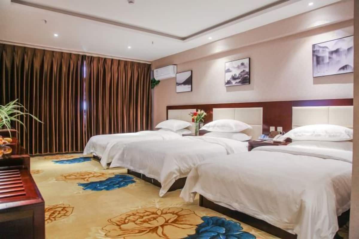 A hotel room with two beds, a piano, and a floral carpet.