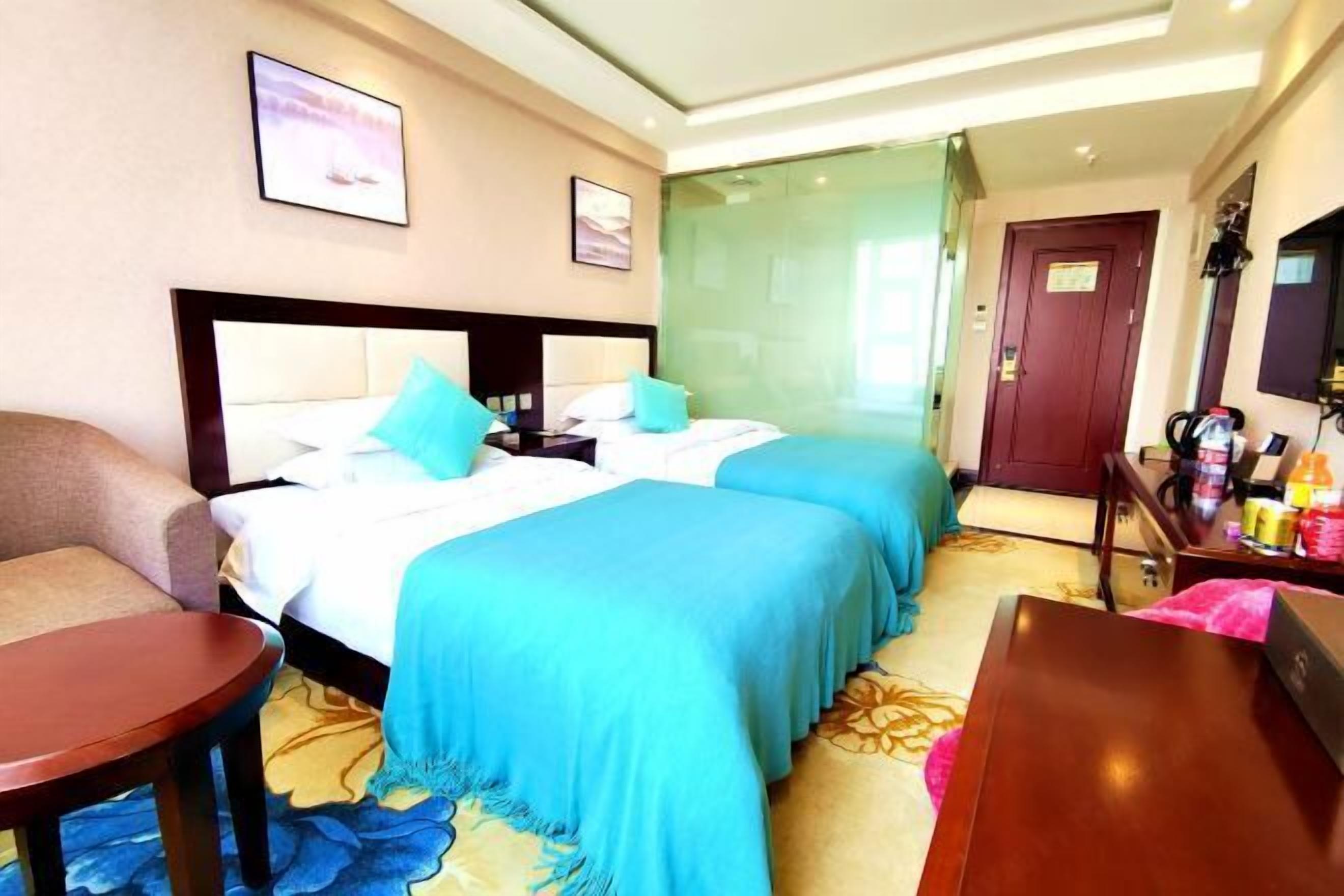 Una habitación de hotel con dos camas, una zona de estar y una puerta que da a un baño.