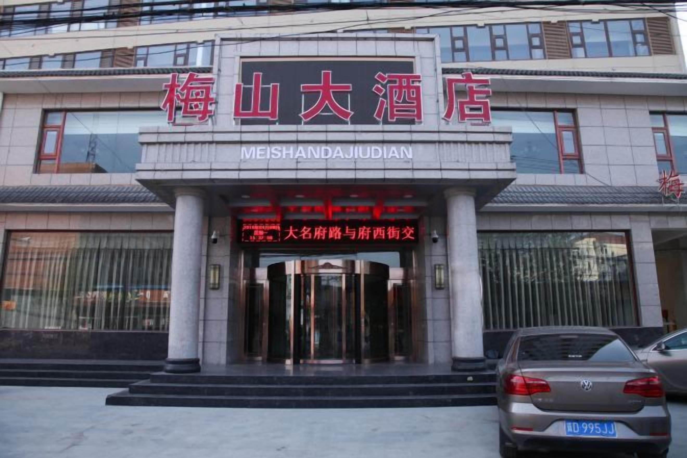 A hotel entrance with a sign indicating 'Meishanda Jiudian' and a red sign with white text.