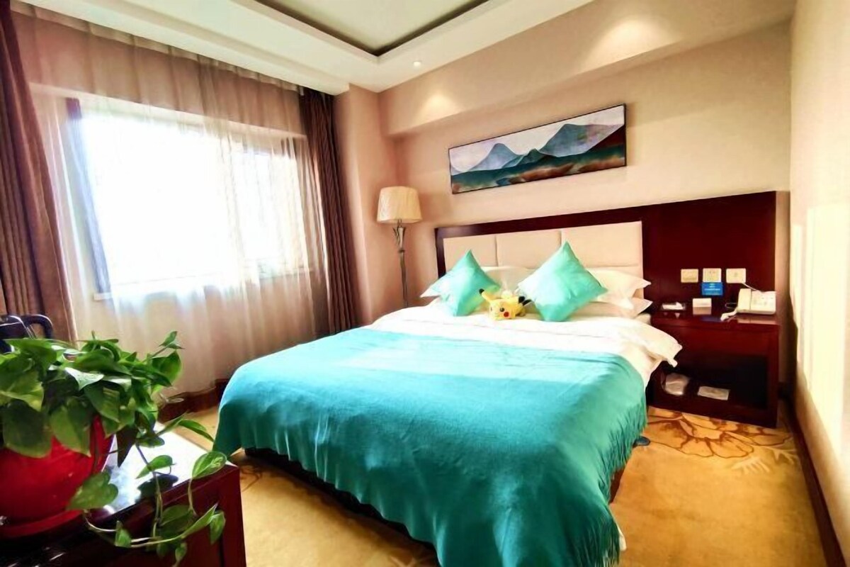 A hotel room with a bed, a desk, a chair, a lamp, and a painting on the wall.