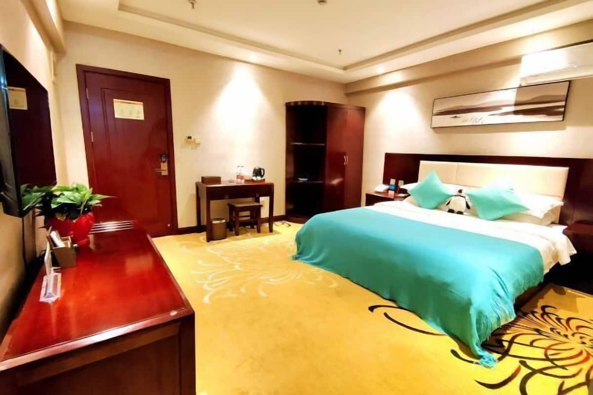A hotel room with a bed, a desk, a wardrobe, and a small table with a plant.