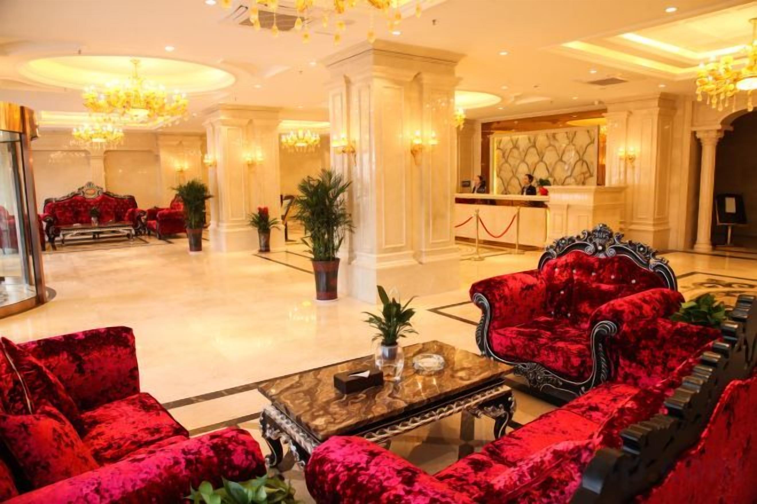 Un hall de hotel con sofás de terciopelo rojo, una mesa de centro de mármol y una recepción.