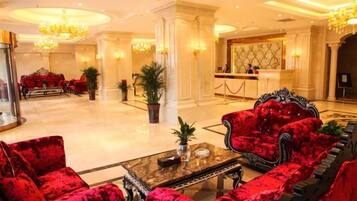 Un hall de hotel con sofás de terciopelo rojo, una mesa de centro de mármol y una recepción.