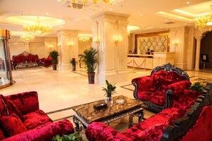 Un hall de hotel con sofás de terciopelo rojo, una mesa de centro de mármol y una recepción.
