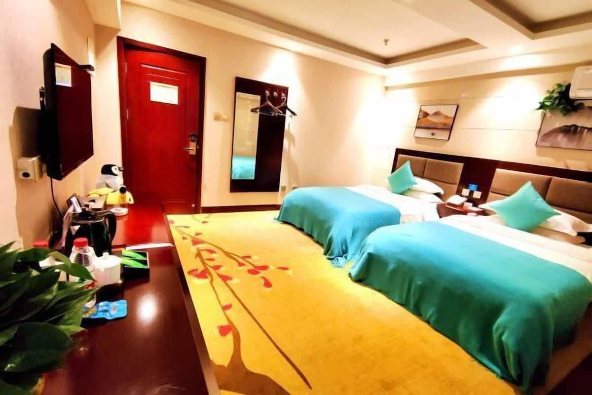 A hotel room with two beds, a desk, a mirror, a TV, and a red door.