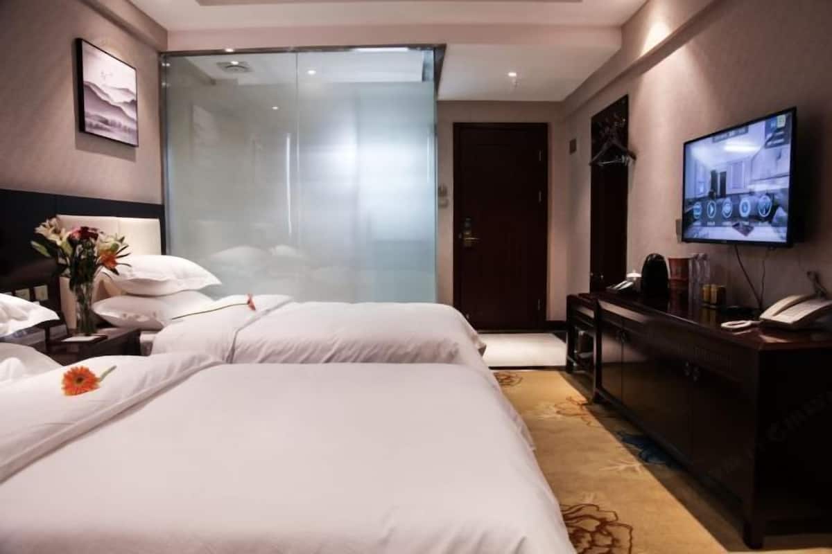 A hotel room with two beds, a desk with a computer, a TV, and a glass partition.