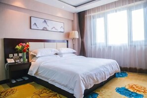 A hotel room with a bed, a nightstand, a lamp, a painting, and a window with curtains. - Meishan Hotel (County Government Store) (Daming)