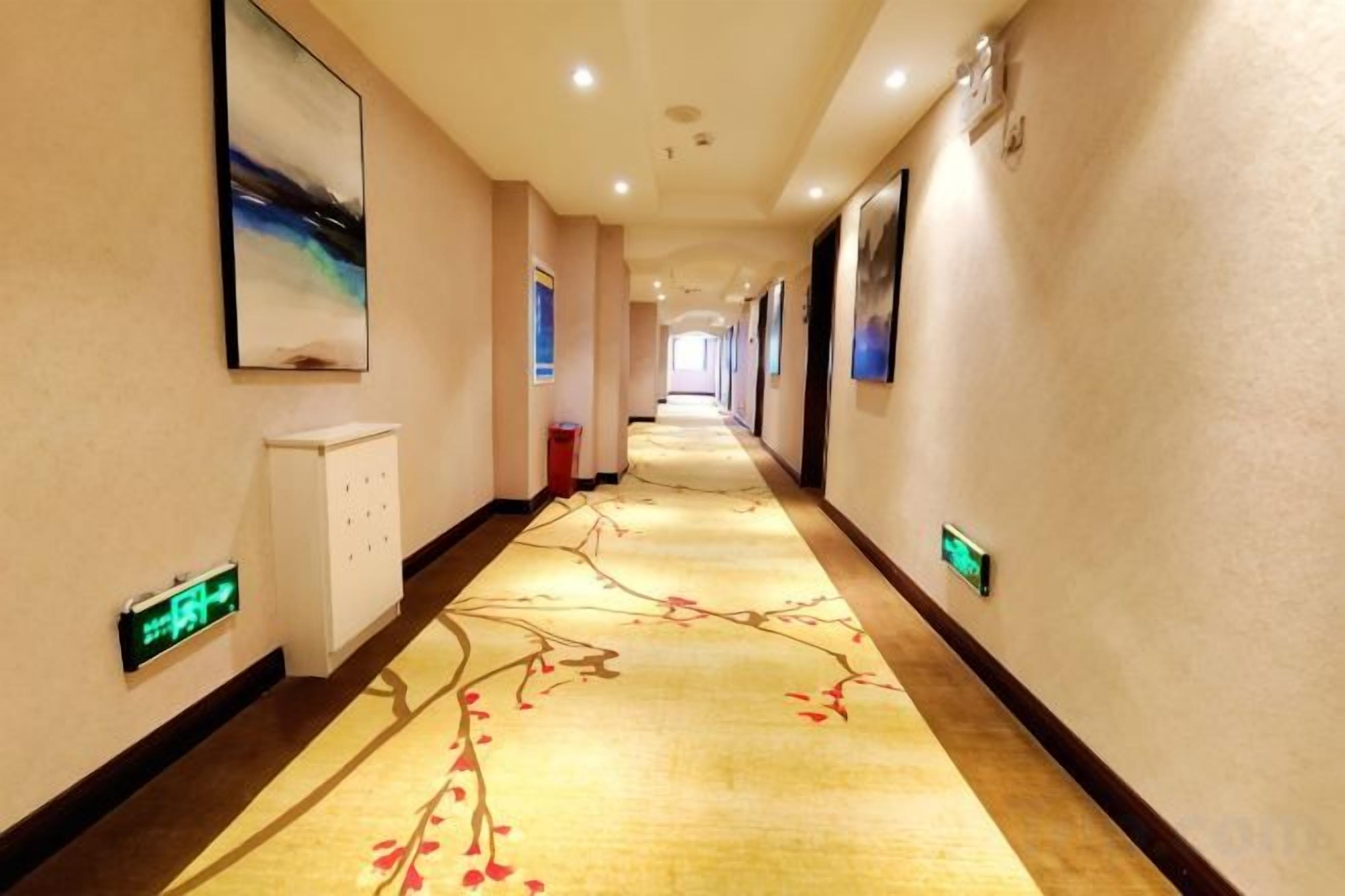 A hotel corridor with a carpeted floor, framed pictures on the walls, and a digital clock.