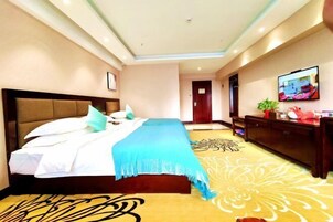 Una habitación de hotel con una cama grande, un cabecero de madera, un televisor de pantalla plana en la pared y una alfombra decorativa.