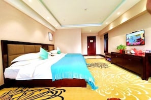 A hotel room with a large bed, a wooden headboard, a flat-screen TV on the wall, and a decorative rug.
