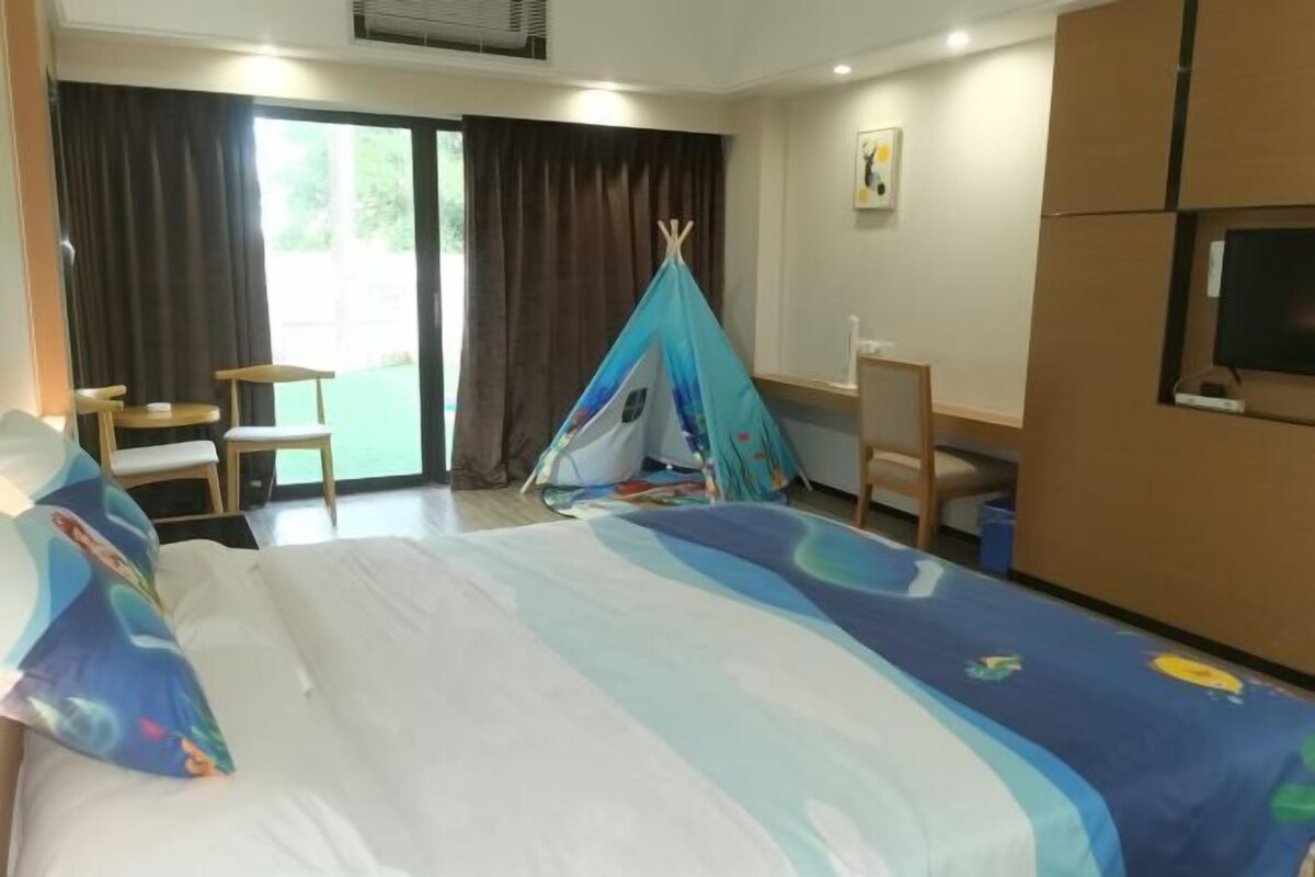 A hotel room with a bed, a desk, a chair, a TV, and a window with curtains.