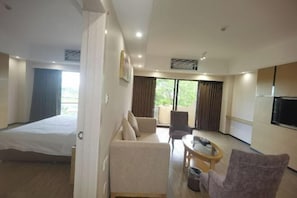 A hotel room with a bed, a sofa, a small table, a chair, and a TV. - Nanhai Hotel (Zhanjiang)