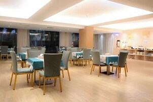 Un comedor amplio con varias mesas y sillas, piso de madera y ventanas grandes.
