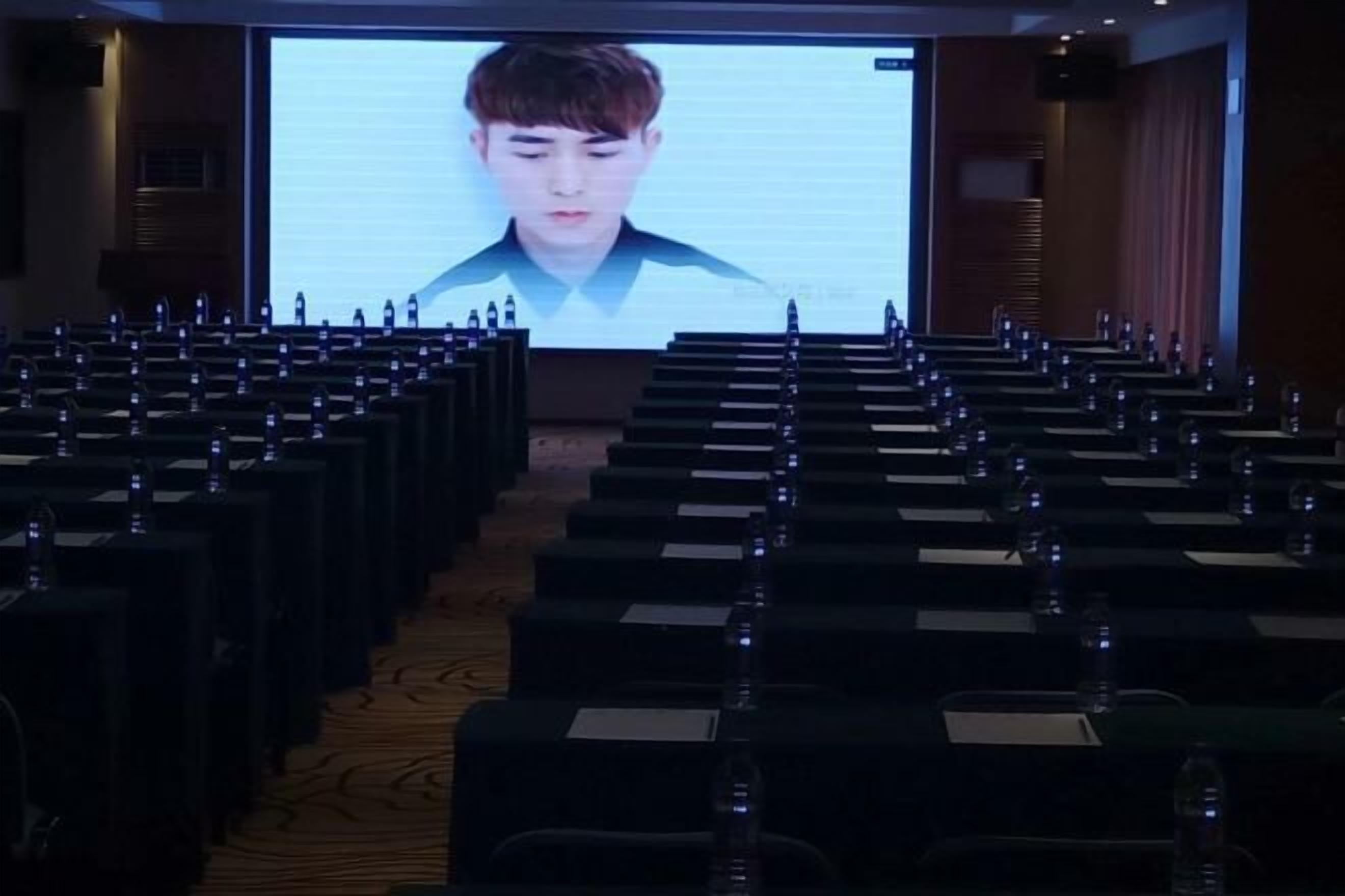 Une salle de conférence avec des rangées de chaises et un grand écran à l’avant.