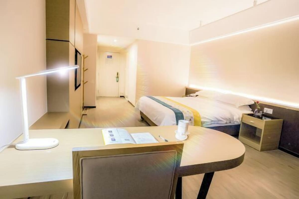 A modern hotel room with a bed, bedside table, and a desk with a chair.