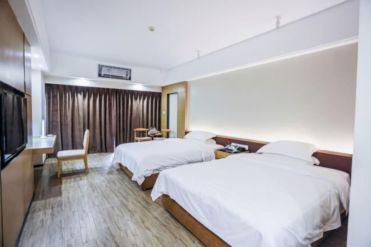 A hotel room with two beds, a desk, a chair, and a TV.