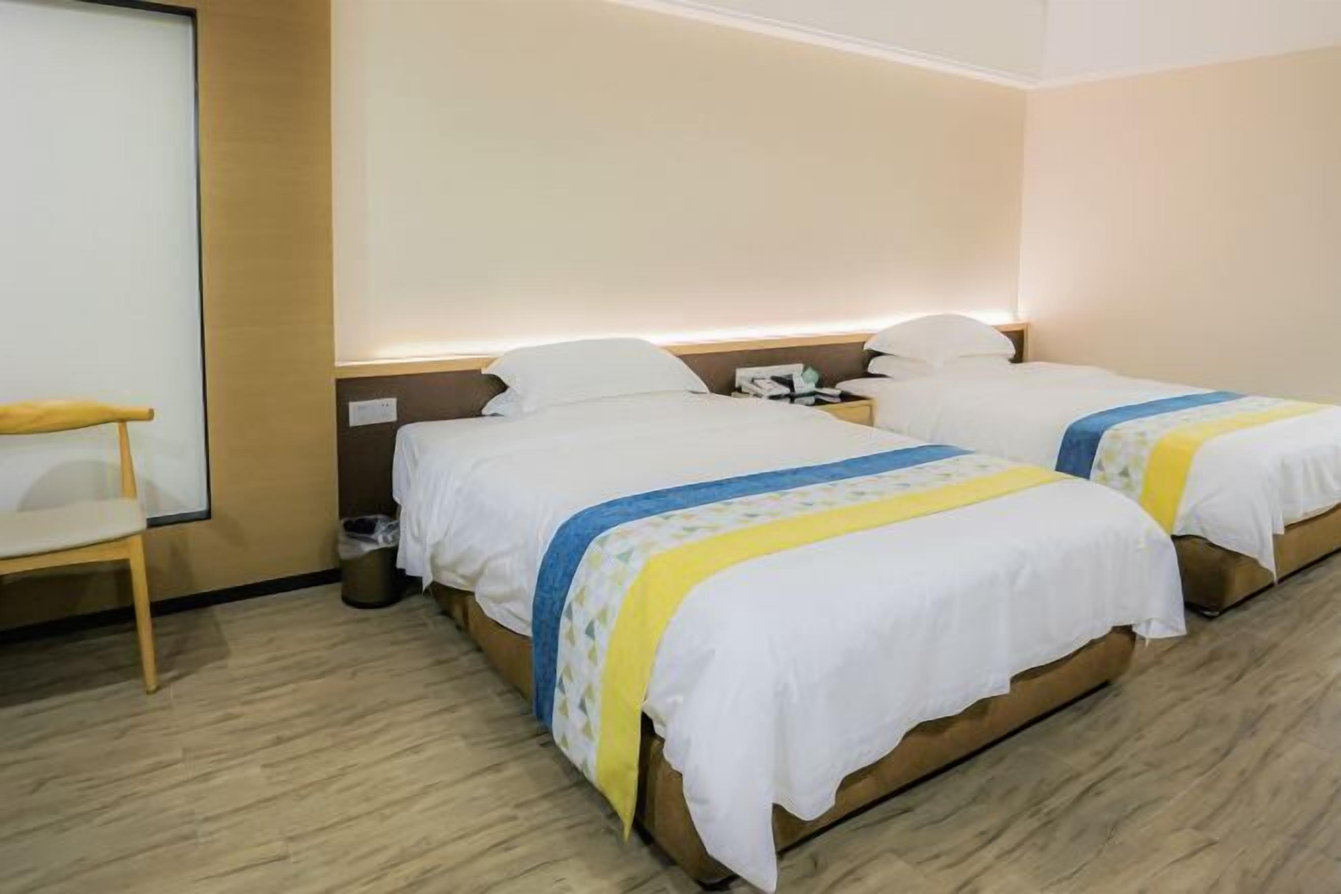 A hotel room with two beds, a wooden floor, a nightstand, and a chair.