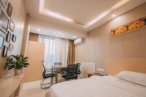 A hotel room with a bed, desk, chairs, a potted plant, and a painting on the wall. - Orange Hotel (Chenzhou)