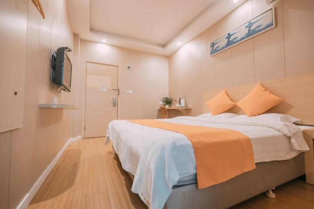 Une chambre d’hôtel avec un lit, une table de chevet, une étagère fixée au mur et une porte.