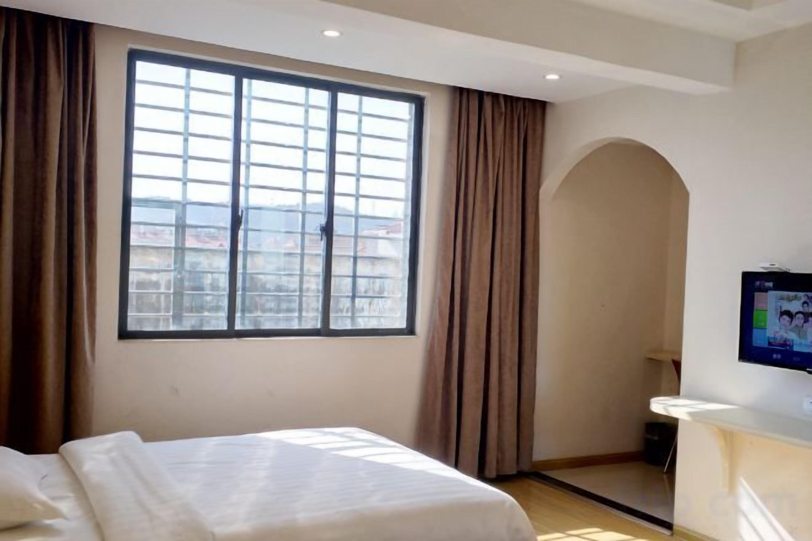 A hotel room with a large window, a bed, a desk, and a TV.