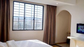 A hotel room with a large window, a bed, a desk, and a TV.