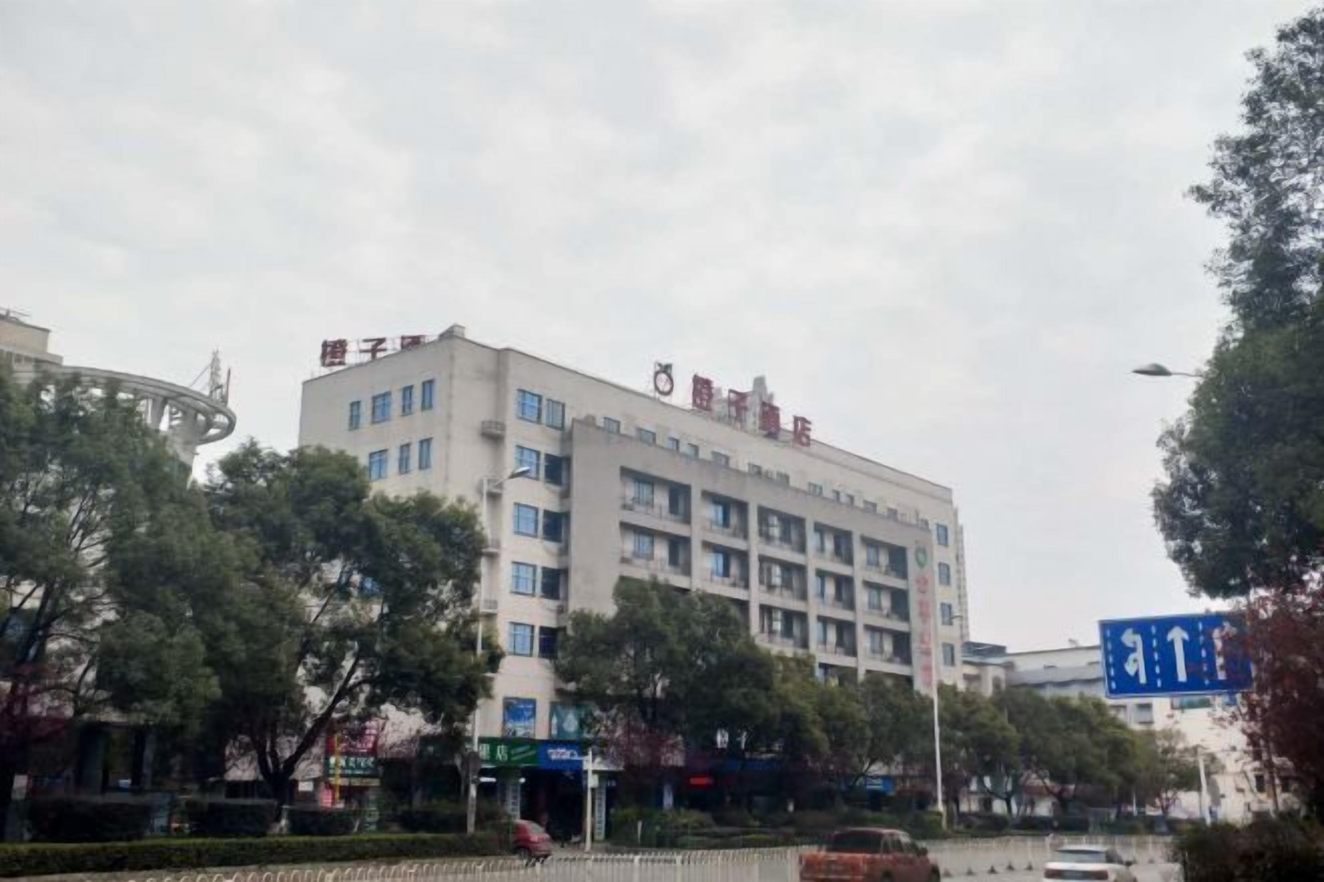 A multi-story building with a flat facade, likely a hotel or office building, with a clear sky and some trees in the foreground.