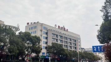 A multi-story building with a flat facade, likely a hotel or office building, with a clear sky and some trees in the foreground.