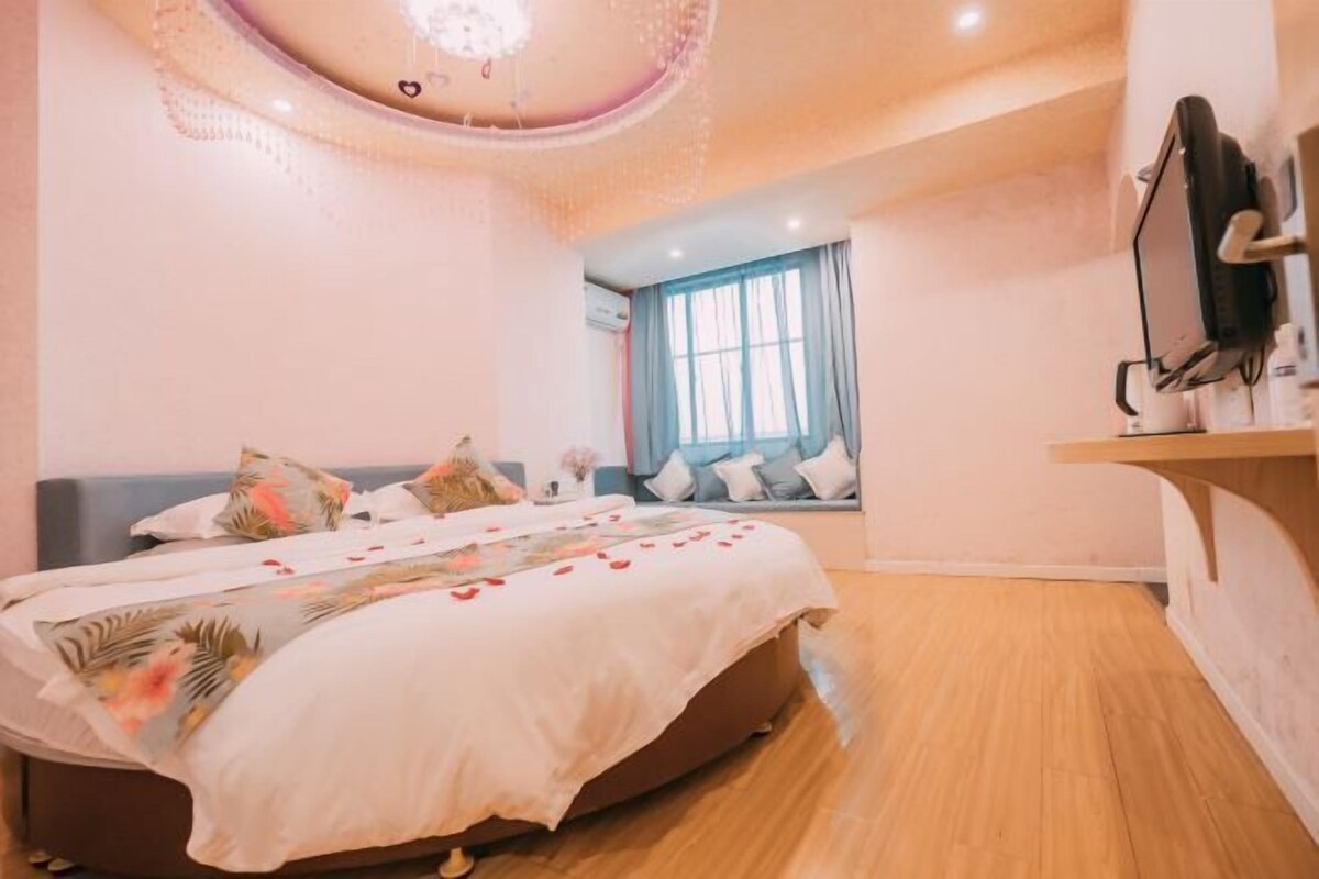 A bedroom with a bed, a window, a TV, and a ceiling light.