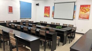 Un salón de conferencias con mesas largas y sillas, una pantalla de proyector y carteles en las paredes.